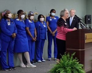 Dr Love at podium with PCTs in blue scrubs