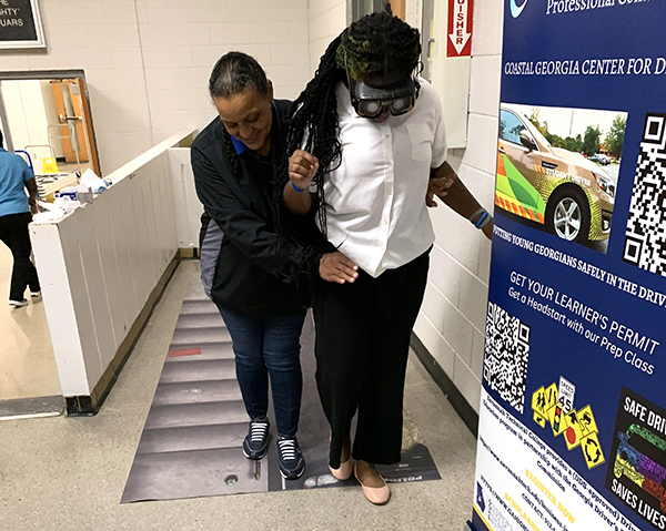 Student wearing VR simulating drunk impairment is assisted.