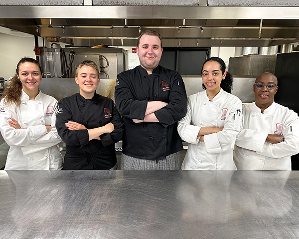 STC students standing in kitchen wearing chef jackets.