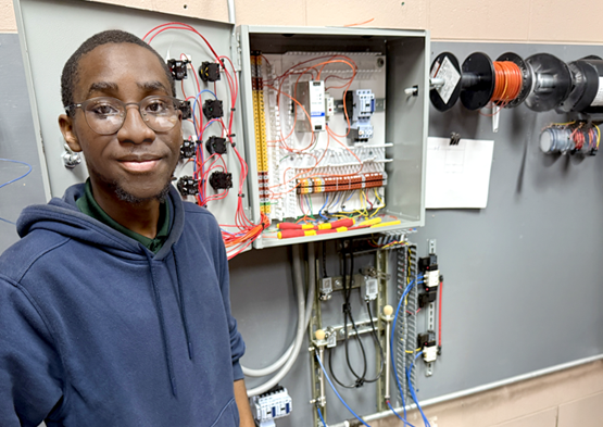Electrical Technology: Electrical technology student stands beside an industrial wiring and controls training panel.