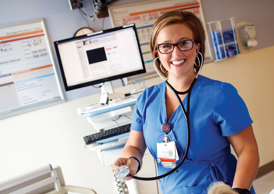 Nursing: Smiling nurse in scrubs holds a stethoscope in a clinical setting.
